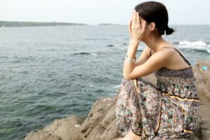 Fille perdue Une femme assise au bord de la mer, le visage dans ses mains, symbolisant la confusion et la perte de repères face à des choix de vie ou au développement personnel.